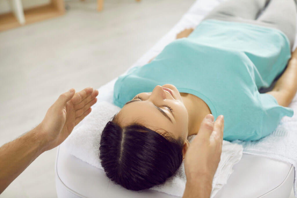 Woman Undergoes Alternative Therapy During Reiki Session In Modern Massage Parlor.